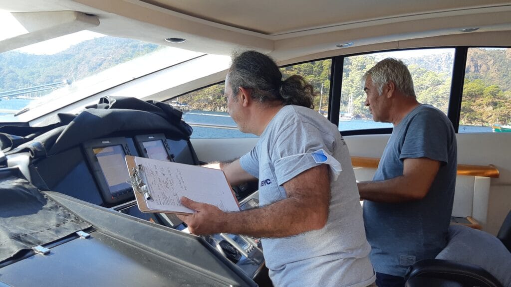 Marine surveyor monitoring engine RPMs, helm controls, and electronic navigation systems during an underway sea trial