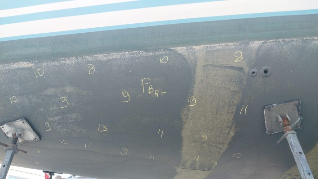 Marine surveyor conducting hull moisture testing and marking readings on a vessel in jackstands
