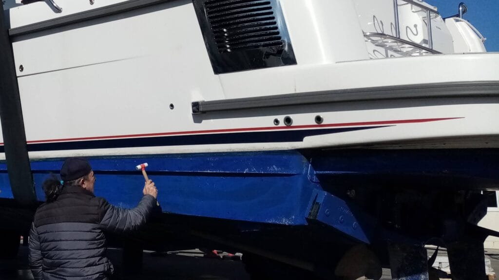 Marine surveyor conducting percussion hammer sounding test on boat hull during structural inspection